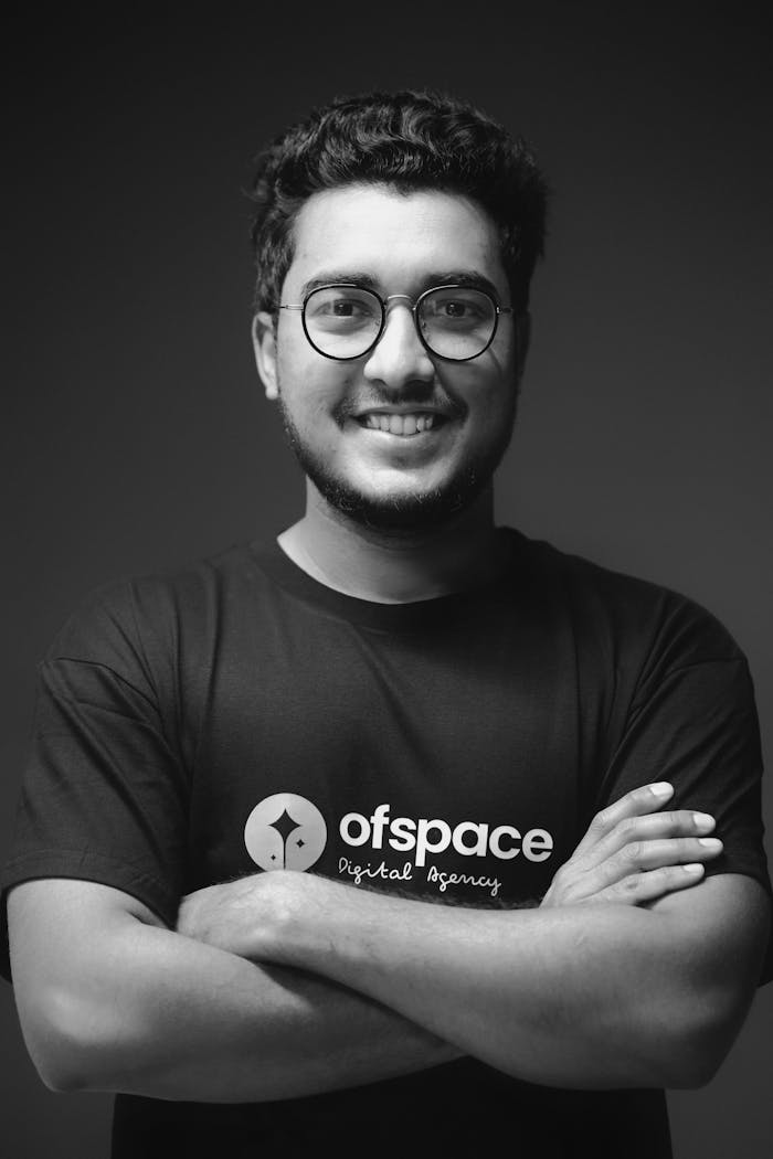 Studio portrait of a smiling young man with eyeglasses in black and white.